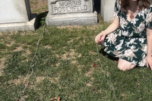 a woman sits on the grass next to a grave which is outlined by thread